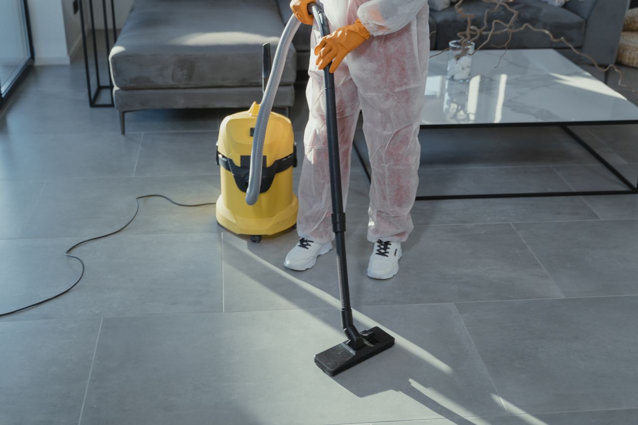A professional cleaner, wearing protective gear, vacuums the floor in a contemporary living room.